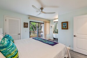 A bedroom with a bed, a ceiling fan, a window with a view of greenery, and a door. - Maui Kamaole, #i215 2 Bedroom Condo by RedAwning (Kihei)