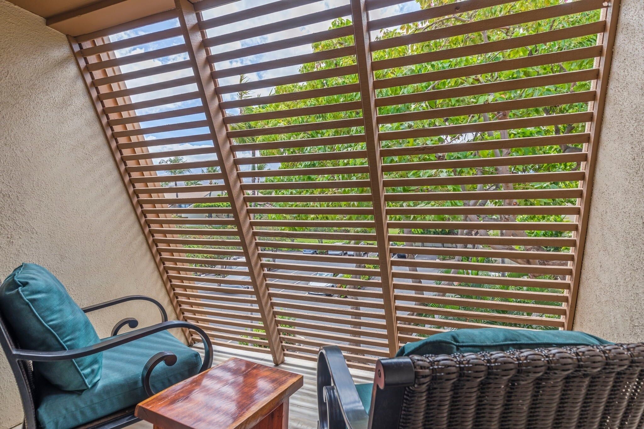 A balcony with a wooden slatted screen, two chairs with cushions, and a small table.