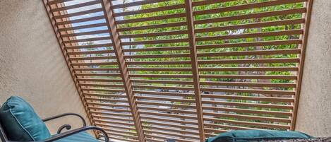 A balcony with a wooden slatted screen, two chairs with cushions, and a small table.