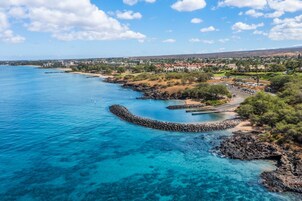 A coastal town with clear blue waters, a rocky breakwater, and residential buildings.