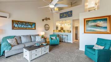 A living room with a sofa, a teal armchair, a coffee table, and a dining area with stools.