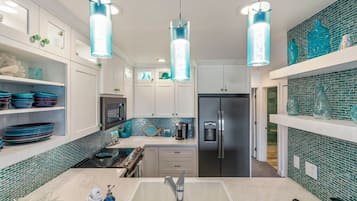 A modern kitchen with a central island, stainless steel appliances, and teal glass pendant lights.