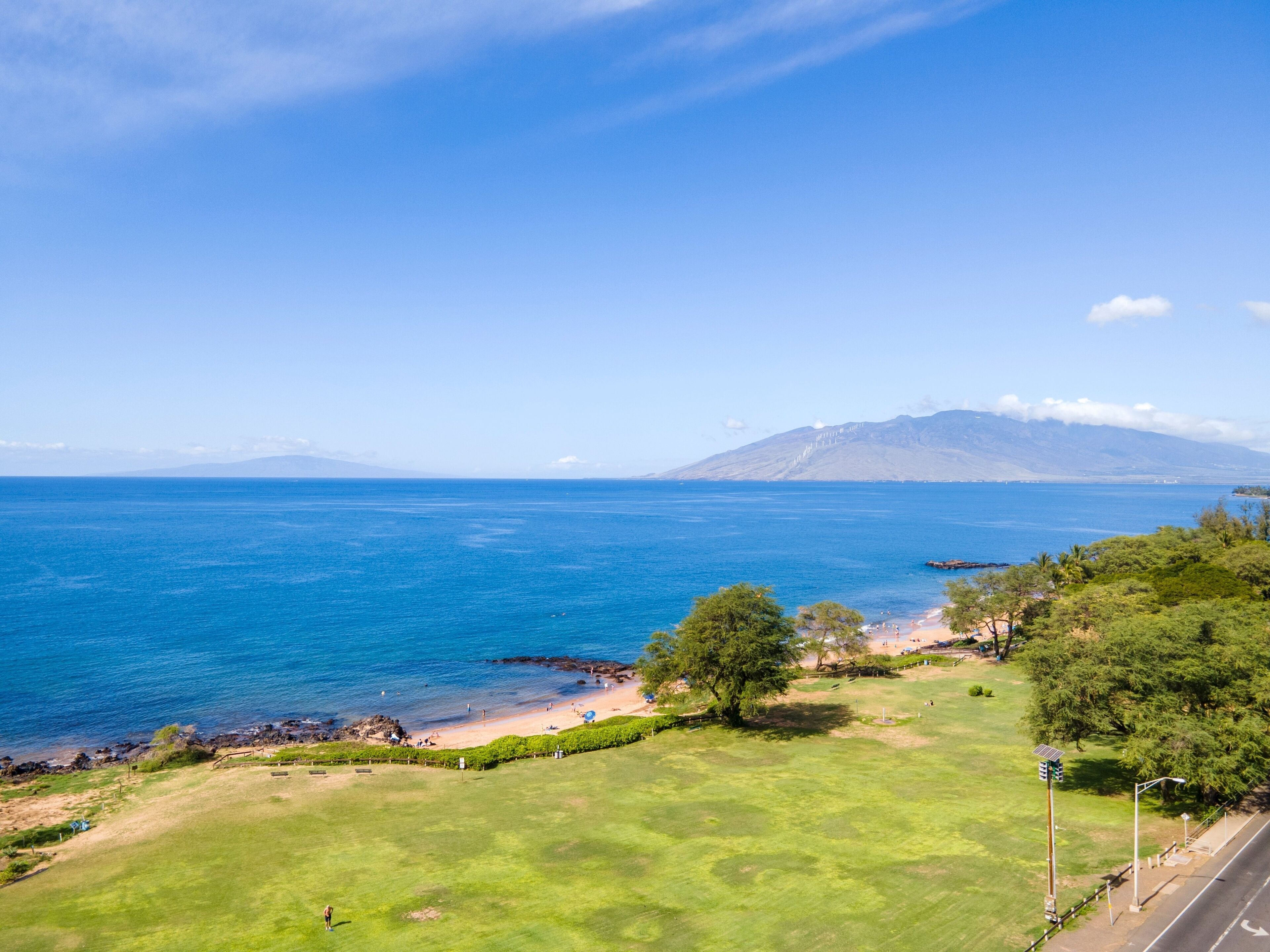 Un paysage côtier offrant une vue dégagée sur la mer, une zone herbeuse et une montagne à l’horizon.