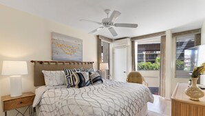 Una camera da letto con un letto, un comodino, una ventola a soffitto, un quadro e vista sull'esterno.