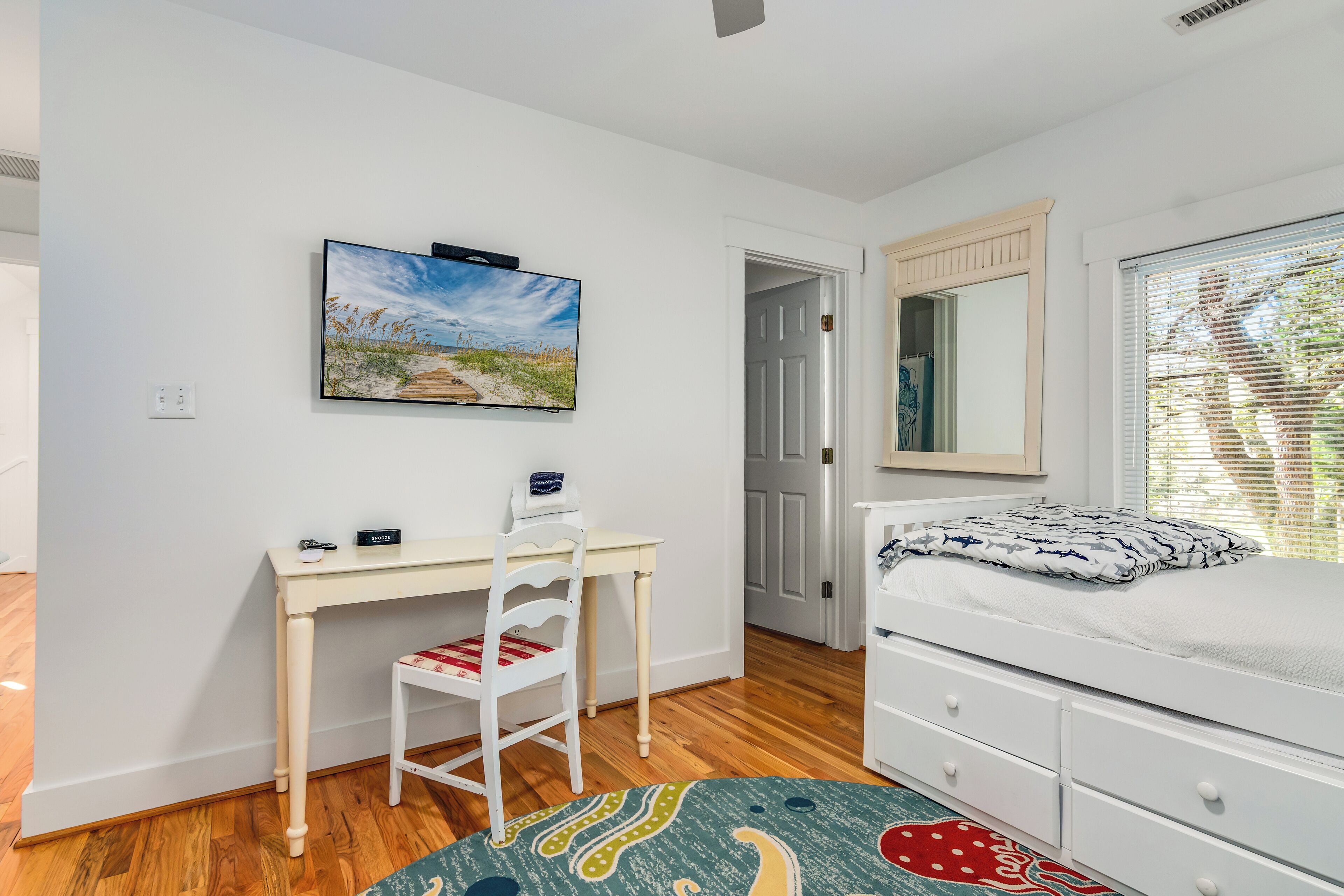 Een slaapkamer met een bed, een bureau, een stoel, een raam met jaloezieën en een schilderij aan de muur.