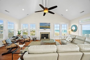 A spacious living room with a fireplace, comfortable seating, and a view of the ocean. - Aqua Vista | Oceanfront 5BR w/ Private Pool, Hot Tub & Stunning Views (Emerald Isle)