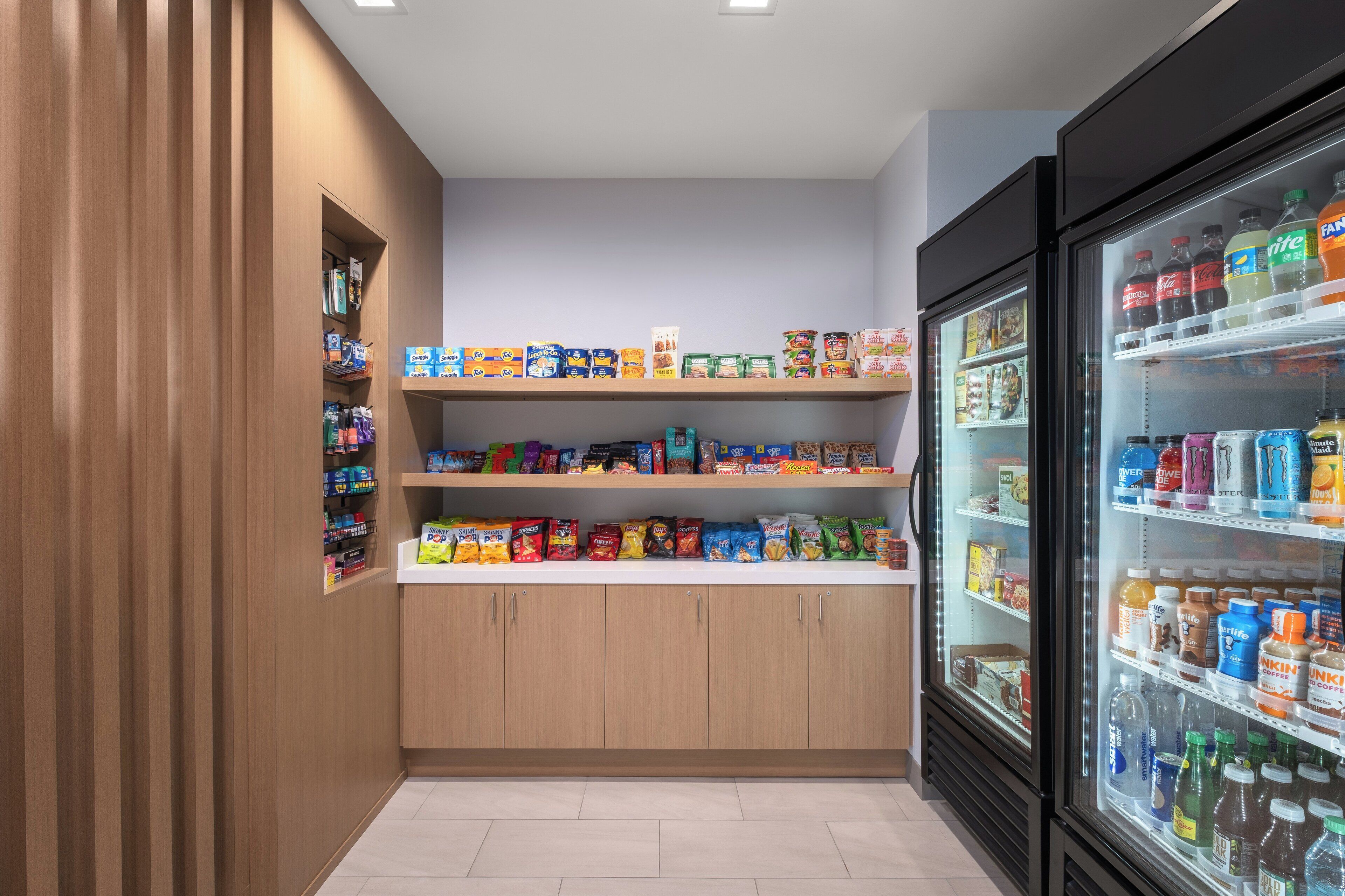 Una sección ordenada y limpia de aperitivos y bebidas, con estantes llenos de diversos productos y un refrigerador.