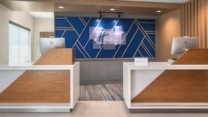 A reception area with a blue and white color scheme, featuring a modern design with geometric patterns on the wall. There are two reception desks with nameplates, and a sign above indicating 'Holiday Inn Express'. - Holiday Inn Express & Suites Buford – Mall of Georgia by IHG (Buford)