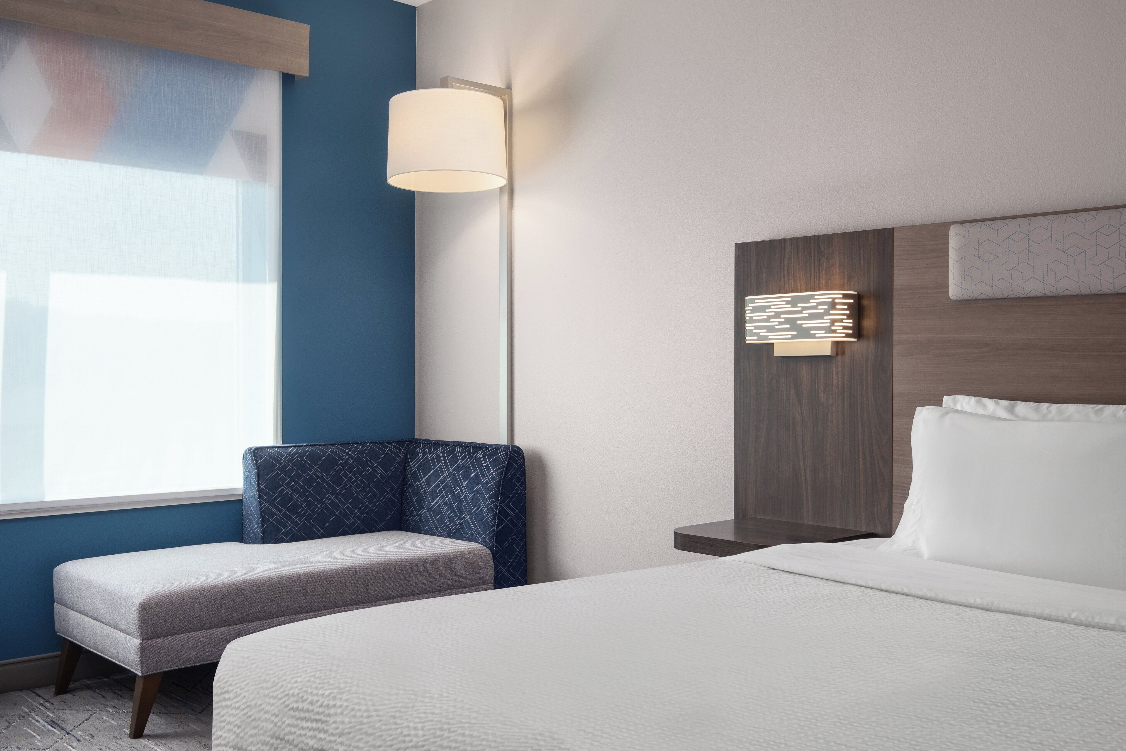 A hotel room with a bed, a seating area, a wall-mounted lamp, and a decorative light fixture.