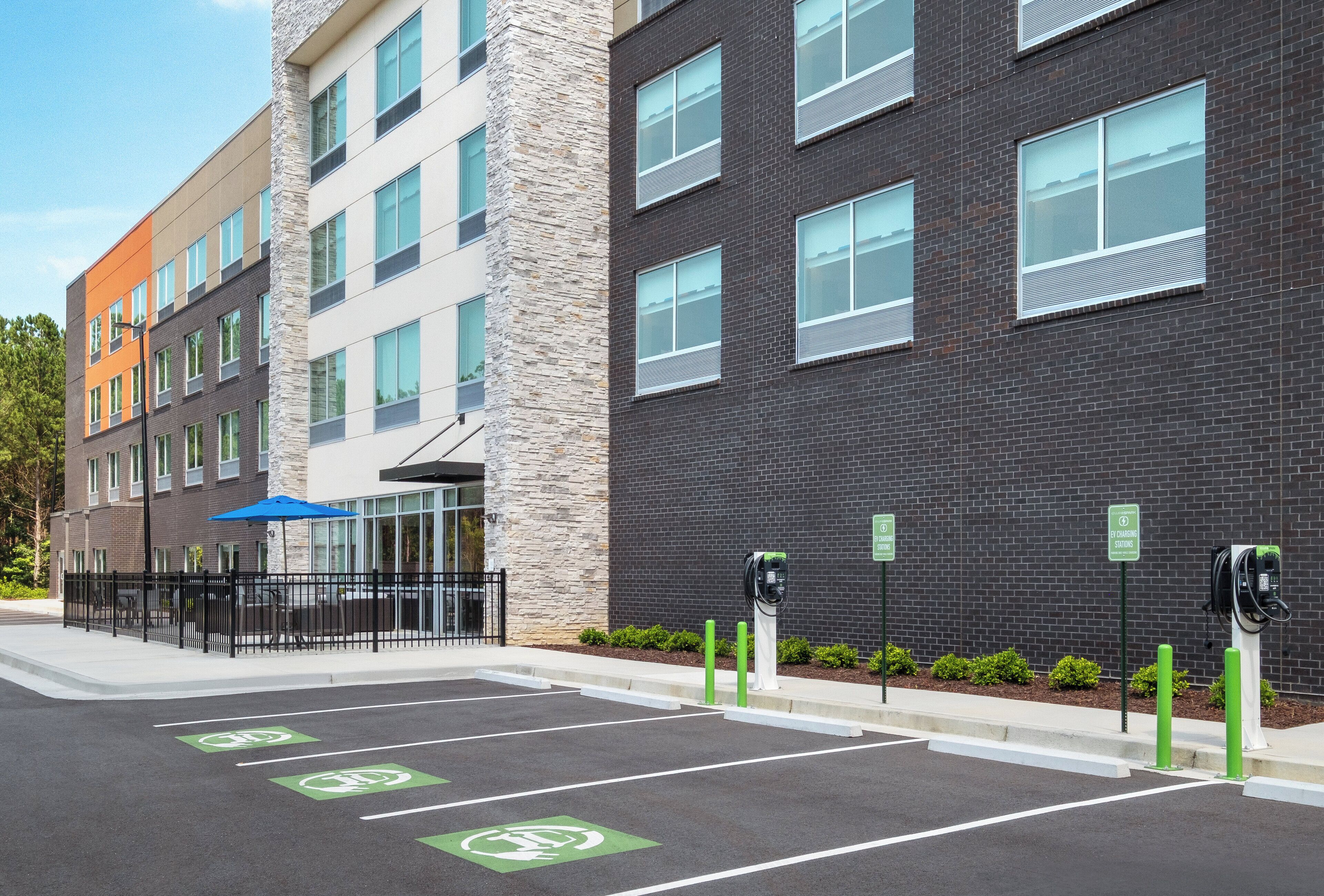 A parking lot with electric vehicle charging stations, a building with multiple floors, and a clear sky.