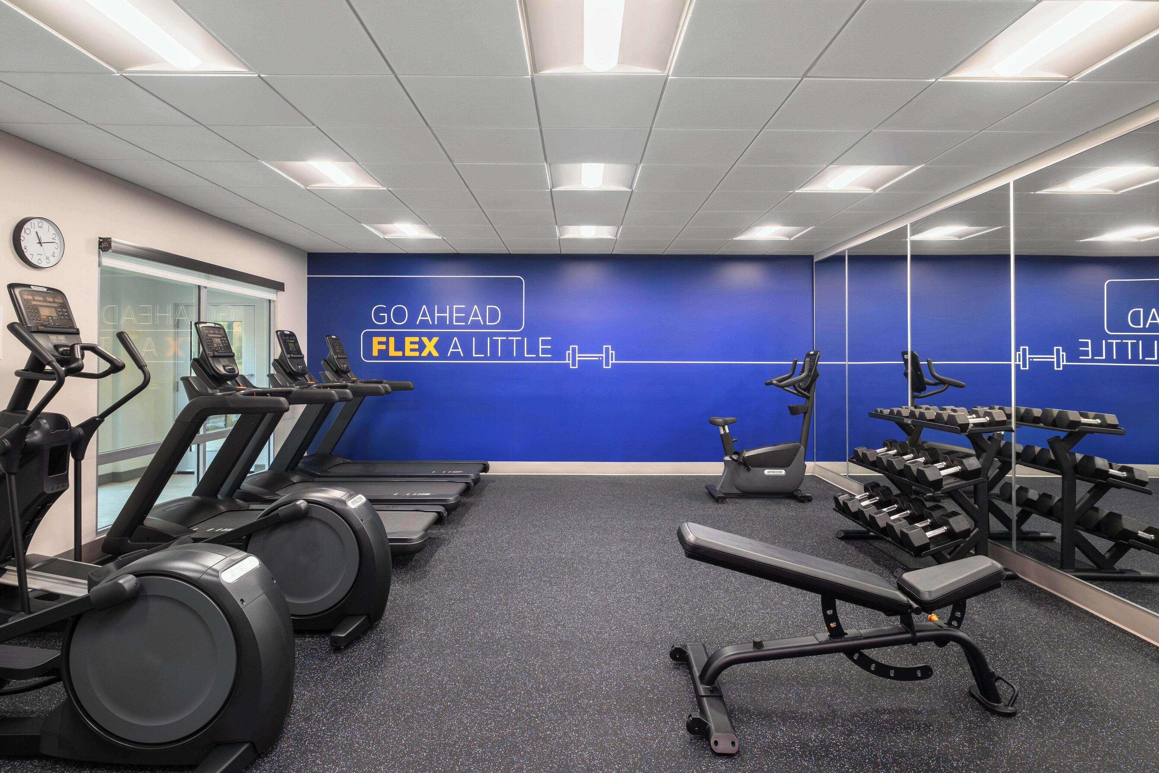 A gym with treadmills, a bench press, and a wall with motivational text.