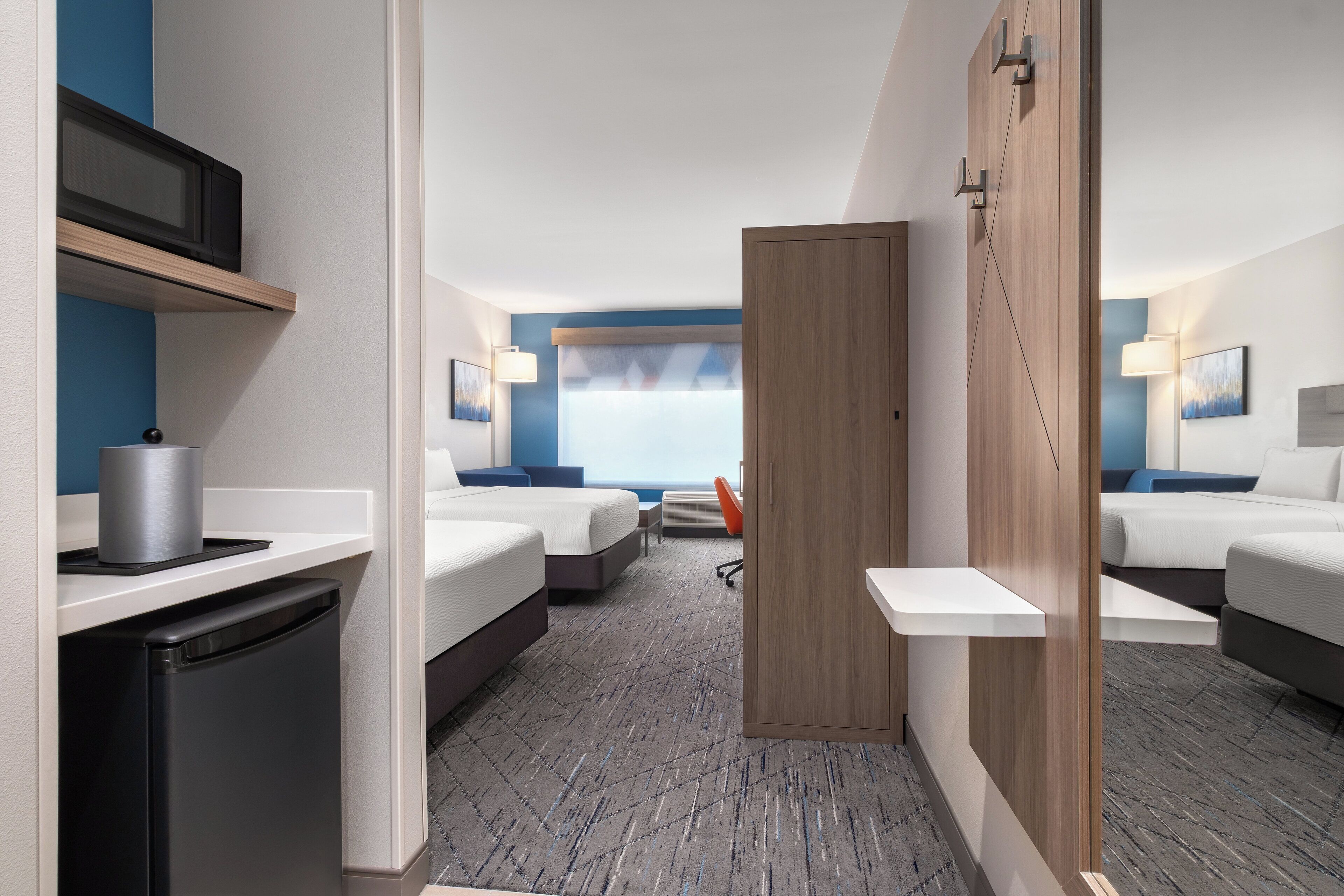 A hotel room with two beds, a desk, a refrigerator, and a microwave.