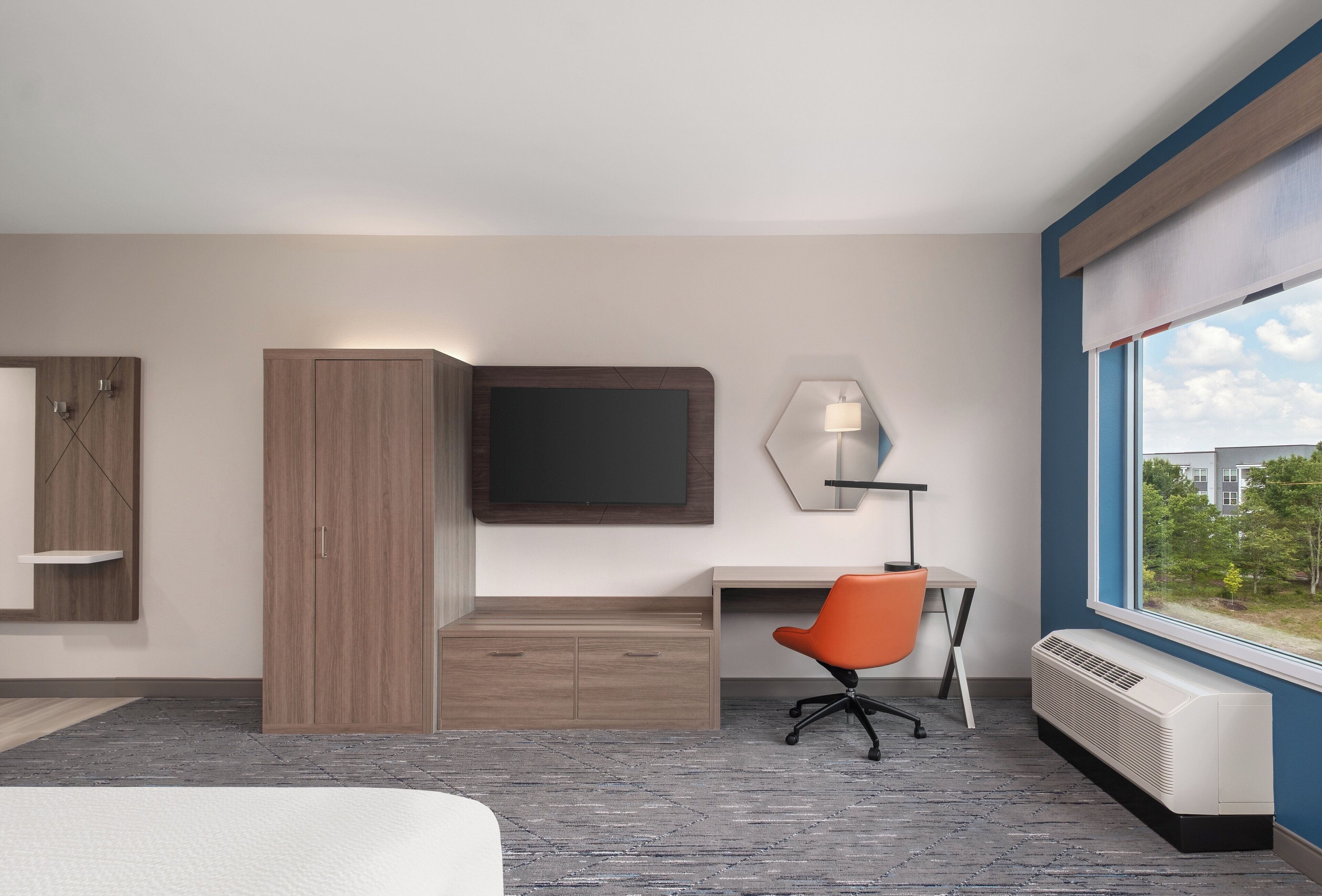 Une chambre d’hôtel comprenant un lit, un bureau, un fauteuil orange, un téléviseur à écran plat, un miroir, un radiateur et une fenêtre donnant sur un paysage verdoyant.