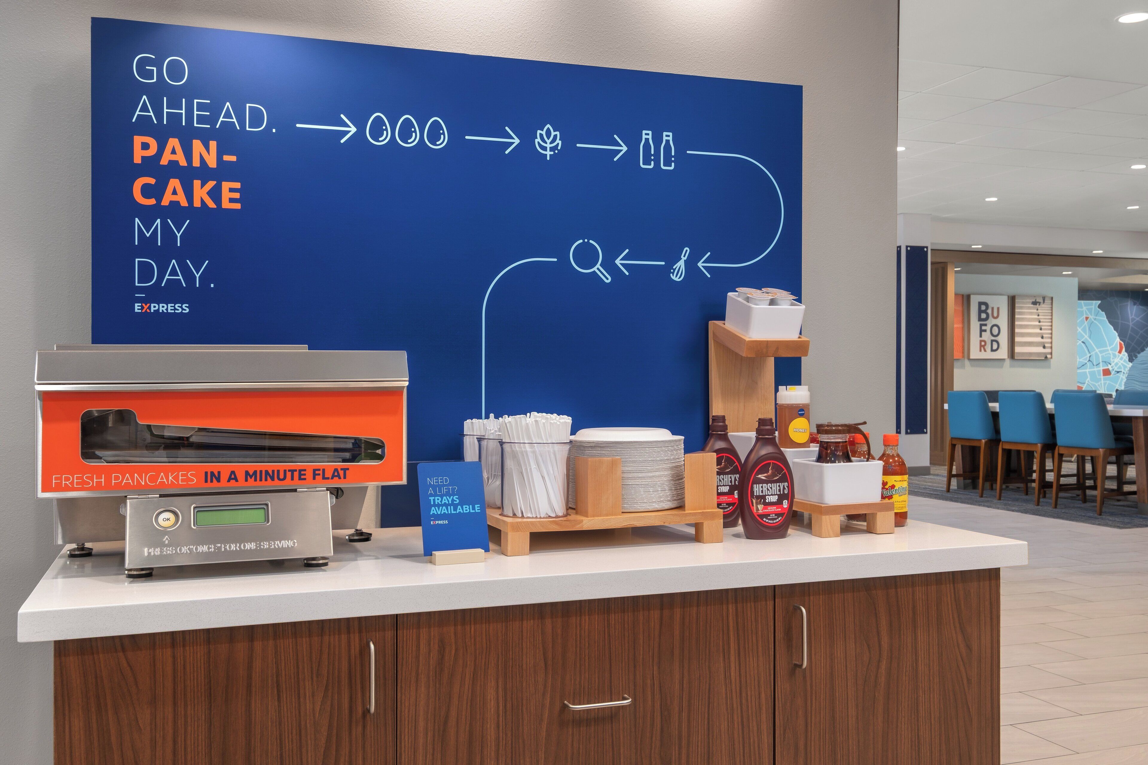 A breakfast station with a sign that reads "GO AHEAD. PANCAKE MY DAY." and a machine for making fresh pancakes.