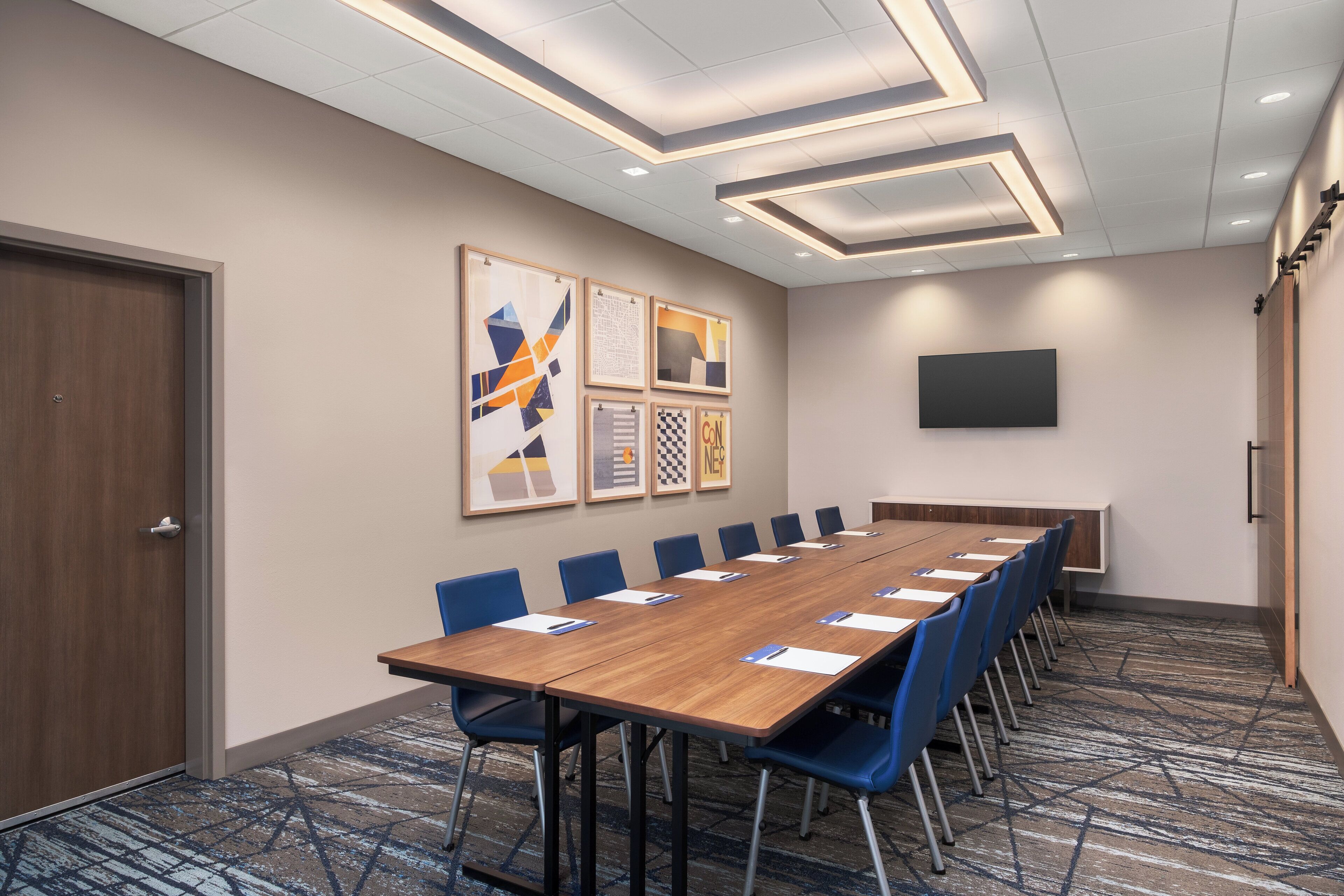 A conference room with a long wooden table, blue chairs, and a patterned carpet.