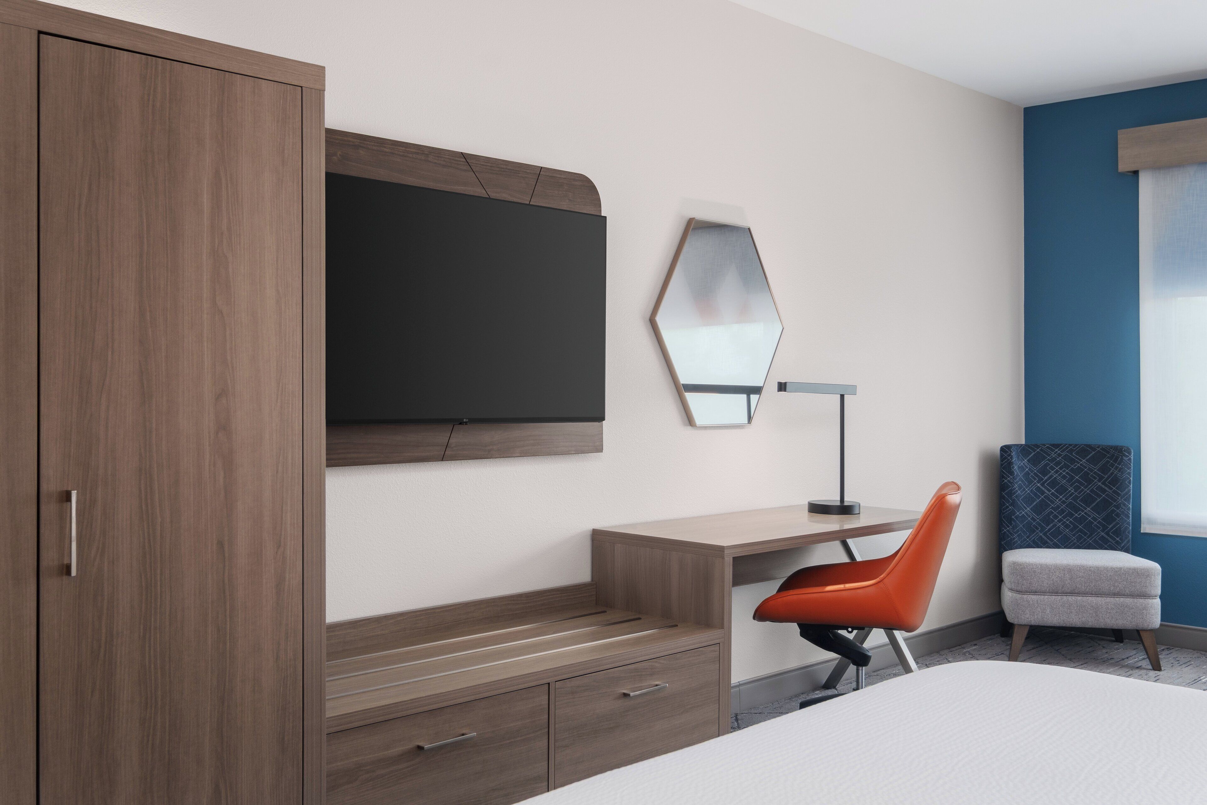 Een moderne hotelkamer met een houten kast, een bureau met stoel, een grote spiegel en een bed.