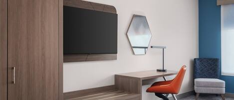 Una habitación de hotel moderna con un armario de madera, un escritorio con una silla, un espejo grande y una cama.