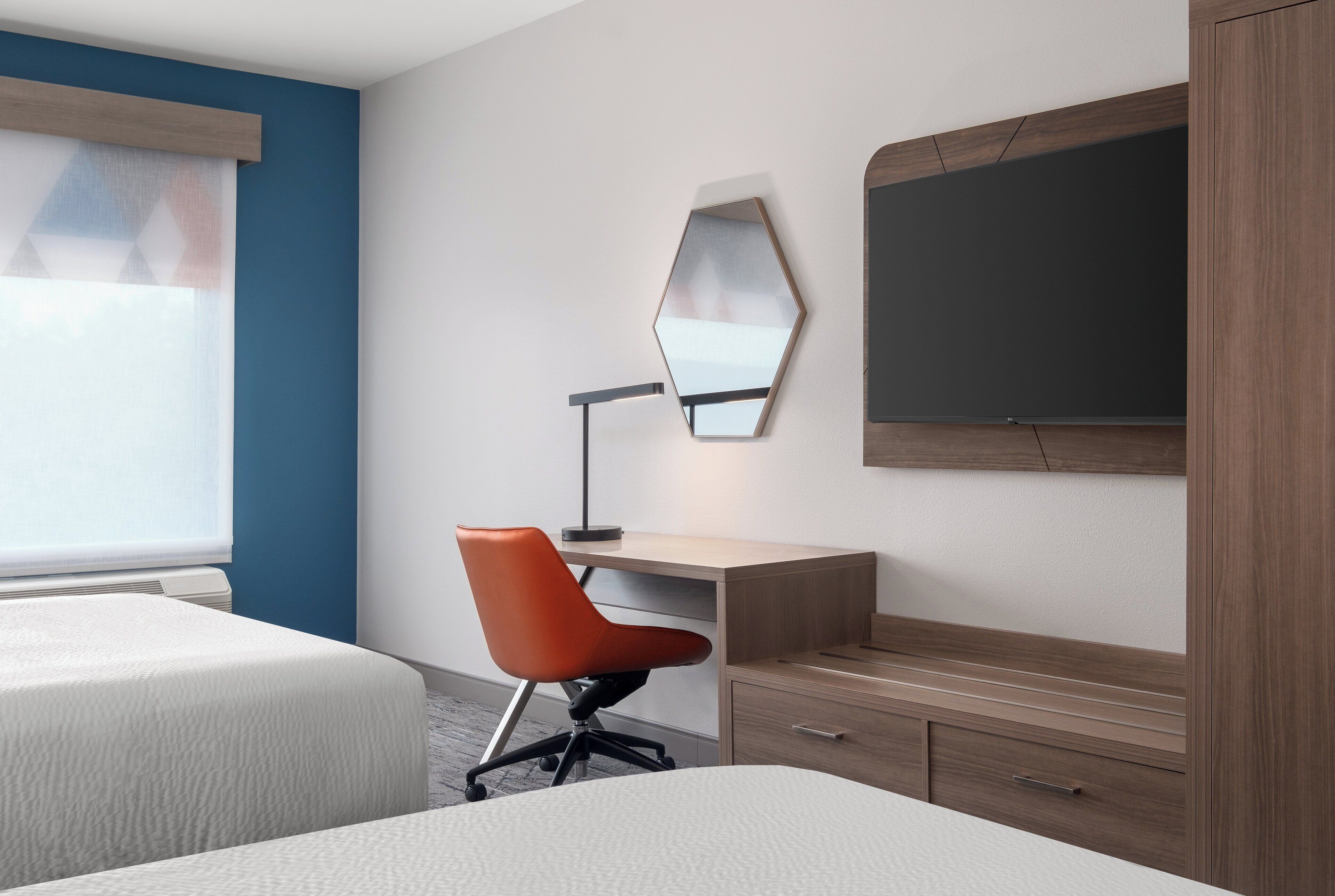 A hotel room with two beds, a desk with a chair, a large mirror, and a wardrobe.