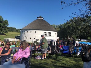 A white building with a distinctive dome roof, surrounded by a grassy area with people seated on chairs.