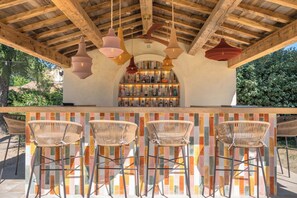 An outdoor bar area with a wooden ceiling, hanging woven light fixtures, and a bar stocked with various bottles.