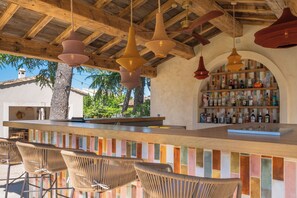 Uma área de bar com cadeiras de vime, teto de madeira e uma prateleira com garrafas.