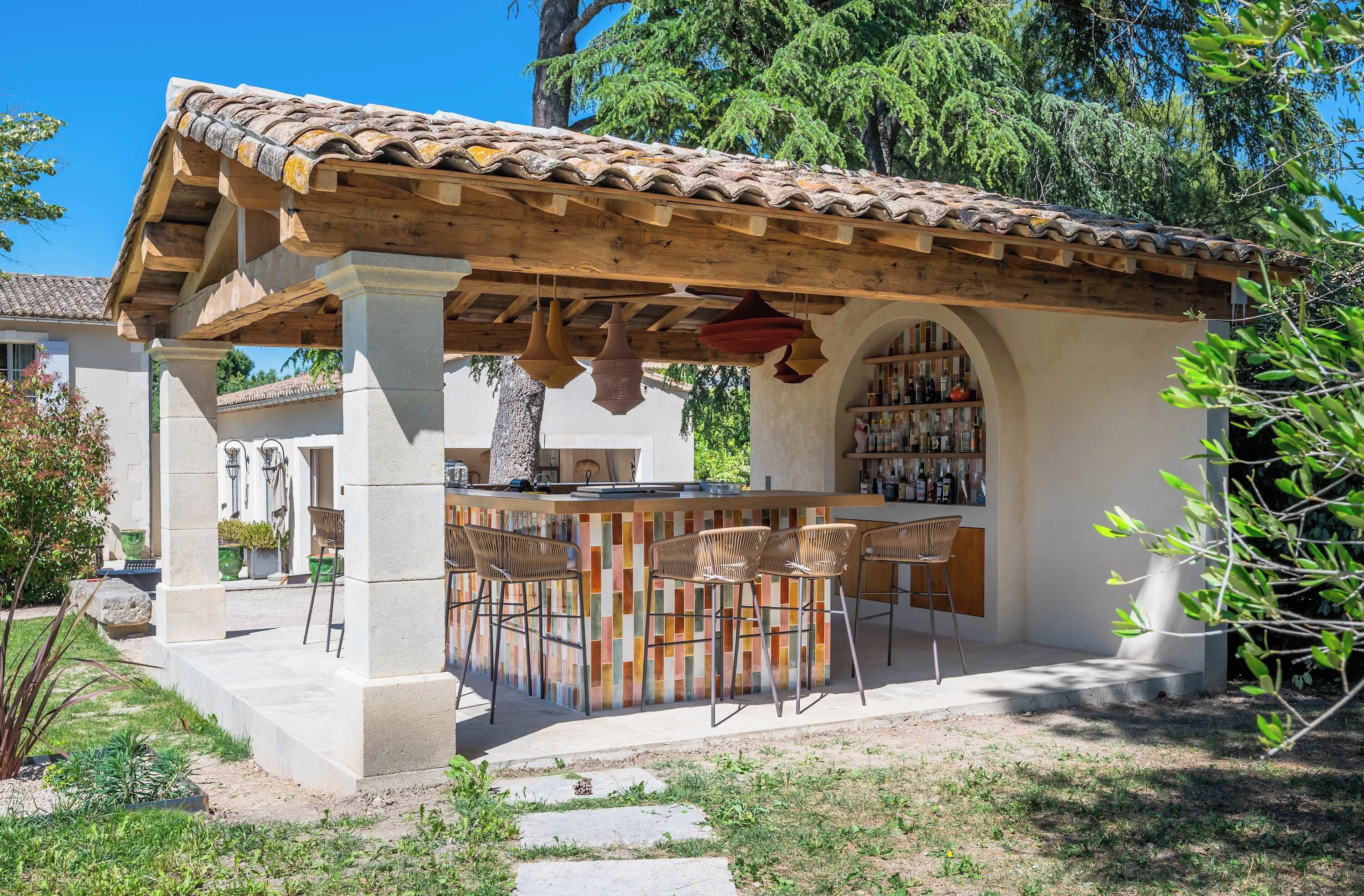 Un área de bar al aire libre con techo de baldosas, pérgola de madera y taburetes de bar.
