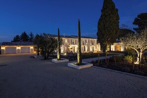 Um edifício bem iluminado, com vários andares, entrada por um caminho e um jardim ajardinado.
