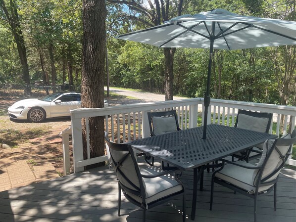 Een terras met een tafel en stoelen, een witte parasol, en een witte auto die in de buurt geparkeerd staat.