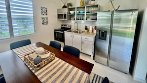 Une cuisine moderne dotée d’appareils électroménagers en acier inoxydable, un coin repas avec une table et des chaises en bois, et une vue sur l’extérieur grâce à de grandes fenêtres.