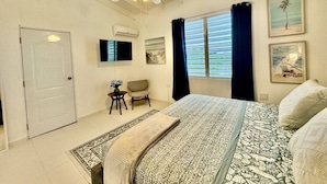 Une chambre à coucher avec un lit, un ventilateur de plafond, une télévision, une fenêtre avec des rideaux et une porte.