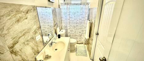 Un baño con pared de mármol, un lavamanos, un inodoro y una cortina de ducha con texto.