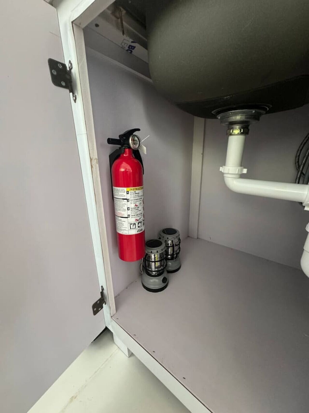 A fire extinguisher mounted on a wall, a water pipe, and two pressure gauges on a white surface.
