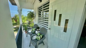 Un balcon avec deux chaises et une table, une porte blanche avec une fenêtre et une rambarde en métal.