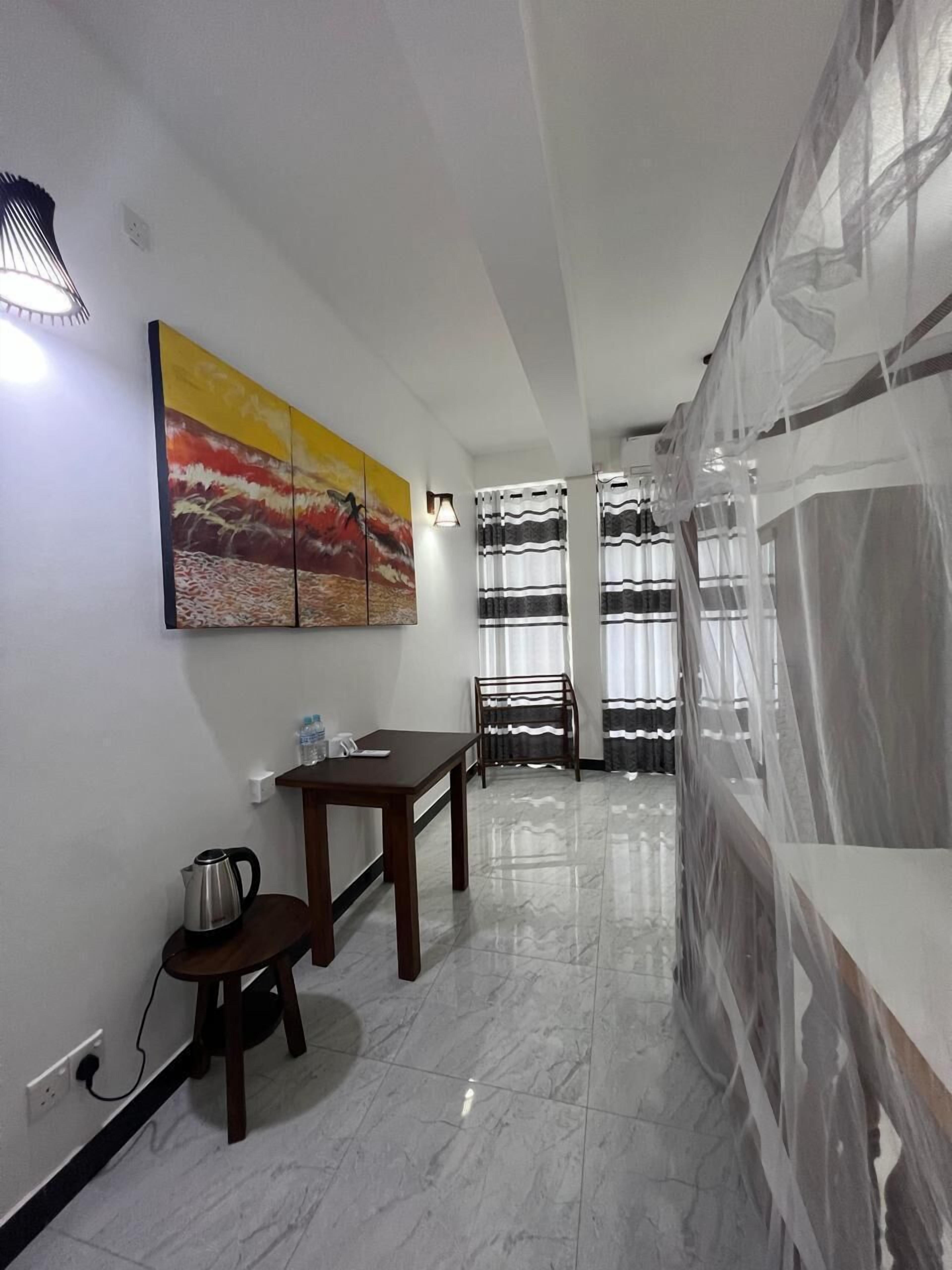 A hotel room with a marble floor, a dining table with chairs, a painting on the wall, and a window with sheer curtains.