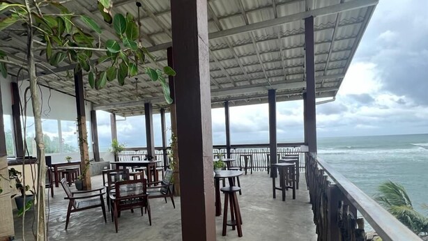 Een terras met tafels en stoelen, een betonnen vloer en uitzicht op de oceaan.