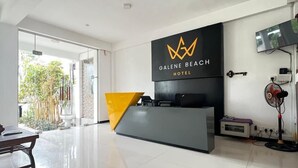 Een moderne hotel receptie met een glazen deur naar een balkon, een receptiebalie en een wandtelevisie.