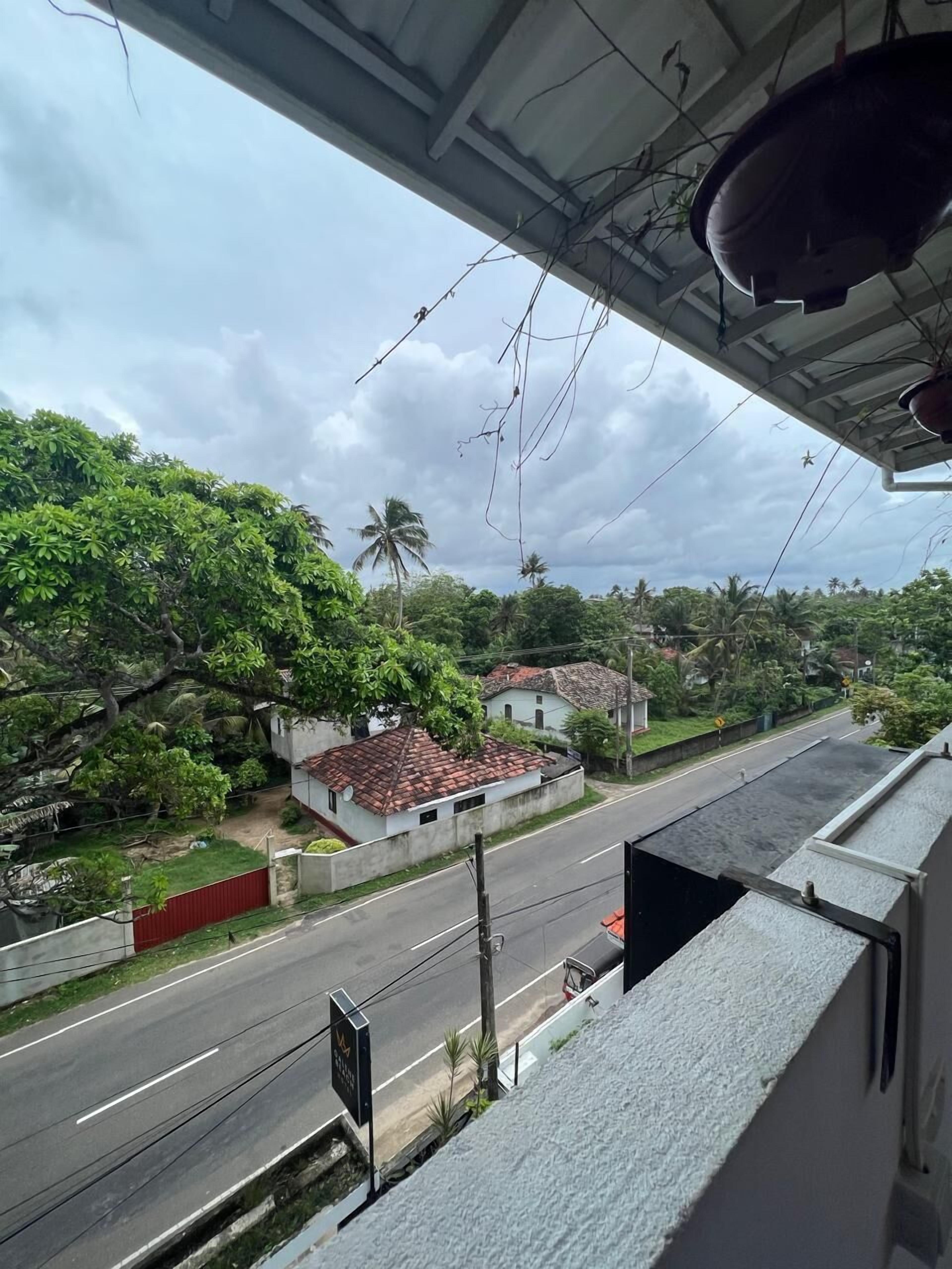 Une vue depuis un balcon donnant sur une rue bordée de maisons et d’arbres, avec un ciel dégagé.