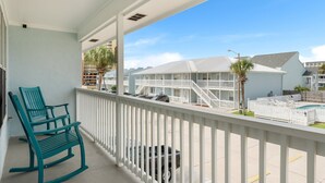 Ein Balkon mit zwei Schaukelstühlen, einem Pool und einem weißen Zaun.