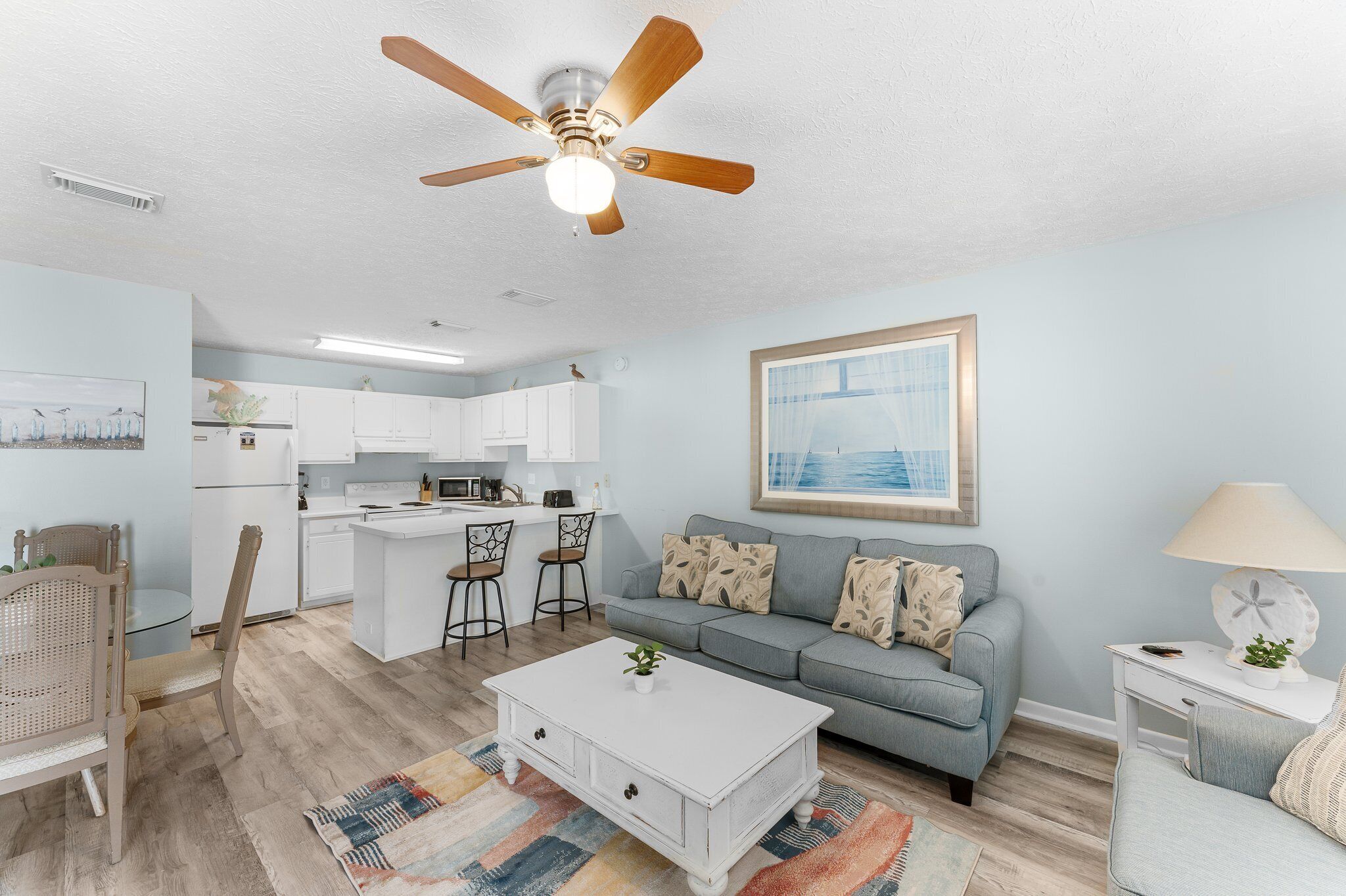 A modern living room with a grey sofa, a white coffee table, and a ceiling fan.