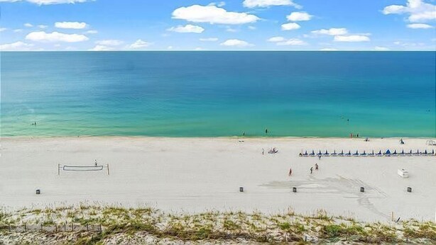 Ein Strand mit blauem Himmel, ruhiger See und wenigen Personen.