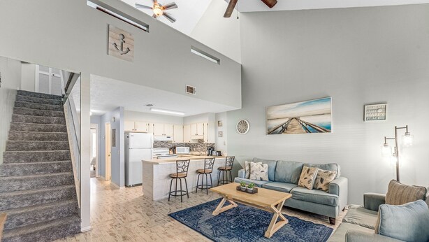 Ein geräumiger Wohnbereich mit Treppe, einer Küche mit Barhocker, einem blauen Sofa und einem Couchtisch.