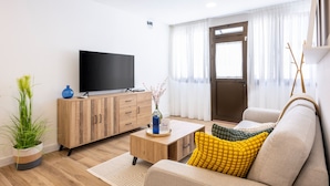 Una sala moderna con televisor de pantalla plana, aparador de madera, sofá y planta en maceta.