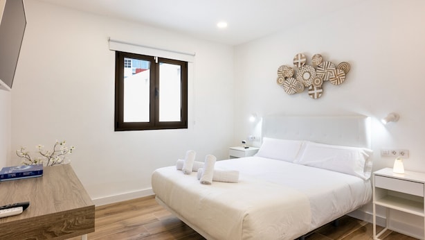 Un dormitorio moderno con una cama grande, una mesita de noche, un televisor y una ventana con persianas.