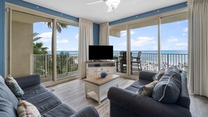 Een balkon met een televisie, zitplaatsen en uitzicht op het strand.