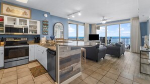 Een moderne keuken met een centraal eiland, een eethoek met uitzicht en een woonkamer met een bank en televisie.