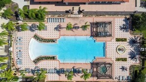Luchtbeeld van een resort met een centraal gelegen zwembad, ligbedden en palmbomen.