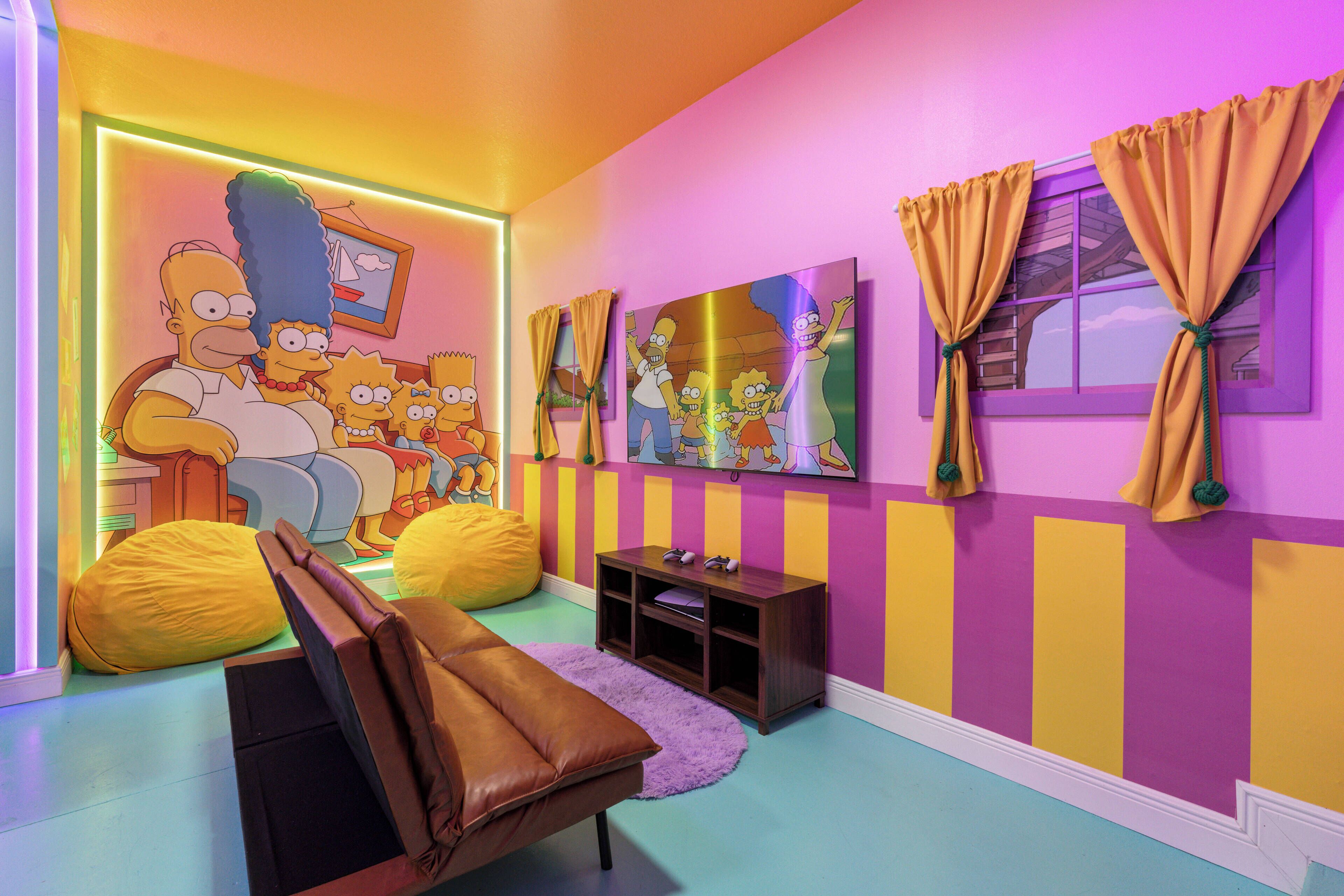 Une pièce aux couleurs vives, ornée d’une grande fresque représentant les personnages des « Simpsons », d’un canapé en cuir marron et d’une petite table d’appoint en bois.