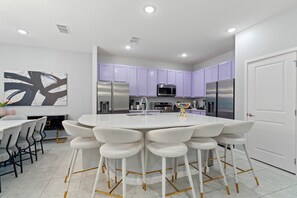 Una cocina moderna con una isla central, taburetes de bar y armarios morados.