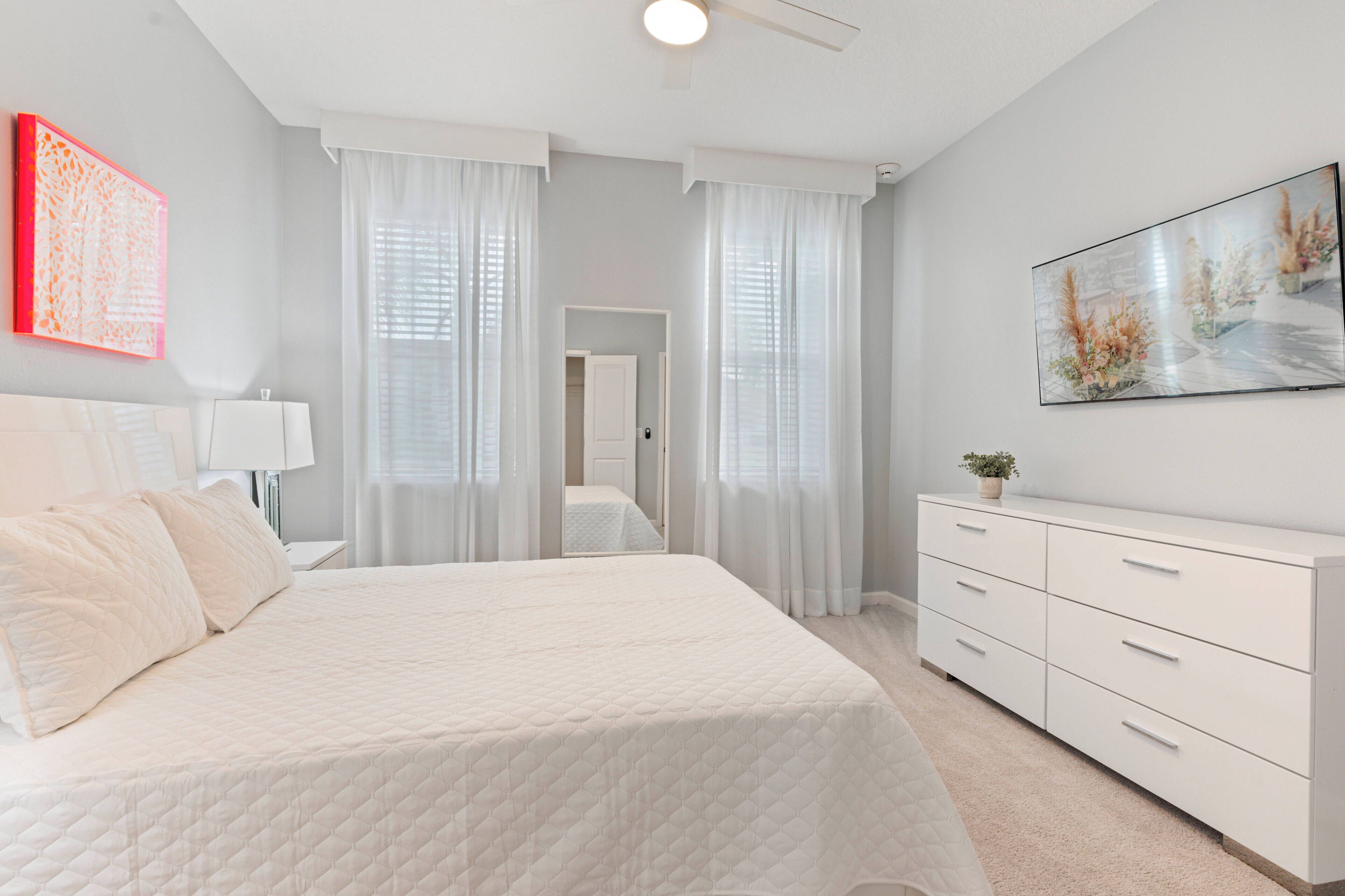 A bedroom with a large bed, a dresser, a nightstand, and a painting on the wall.
