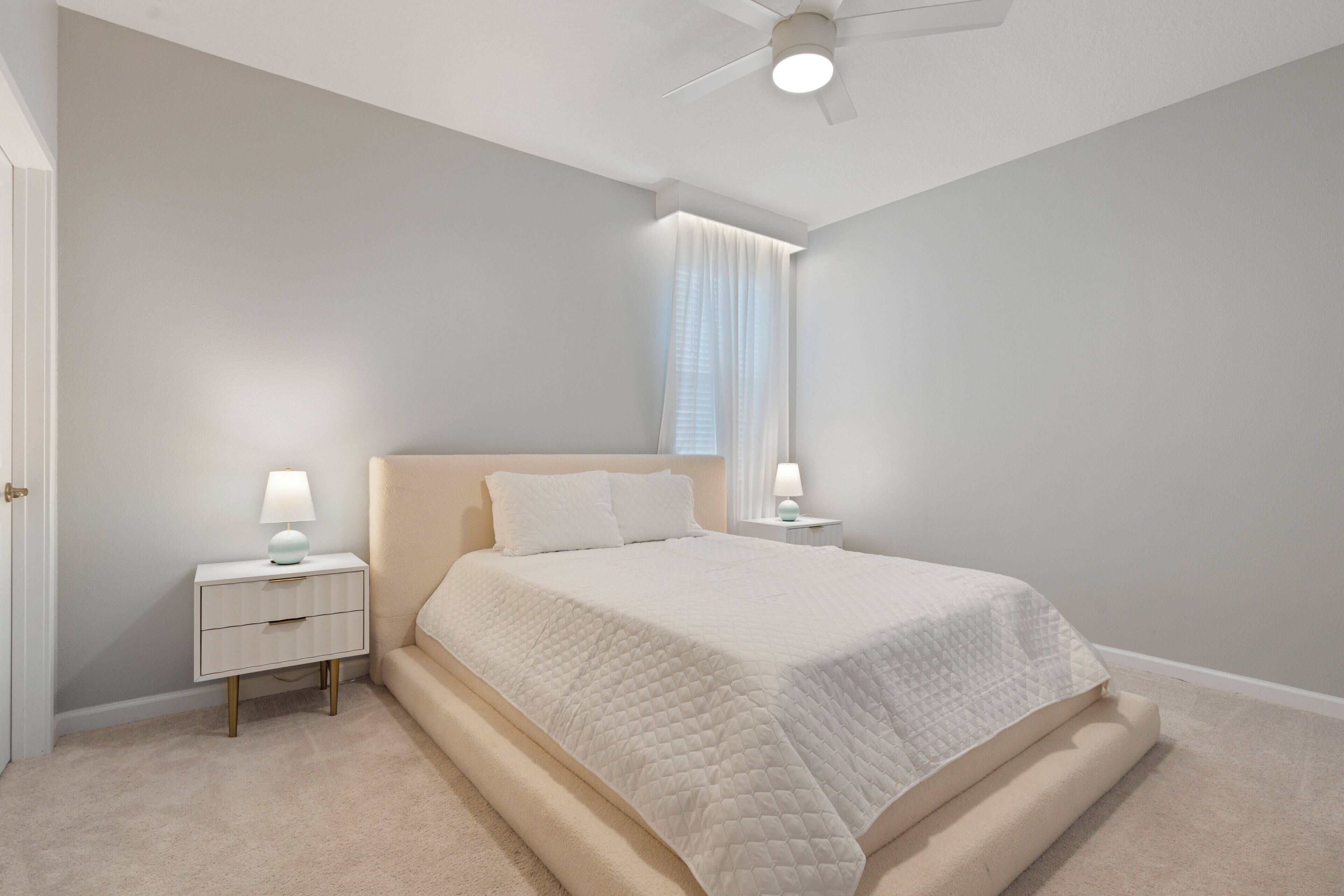 A bedroom with a bed, bedside tables, a ceiling fan, and a window with curtains.